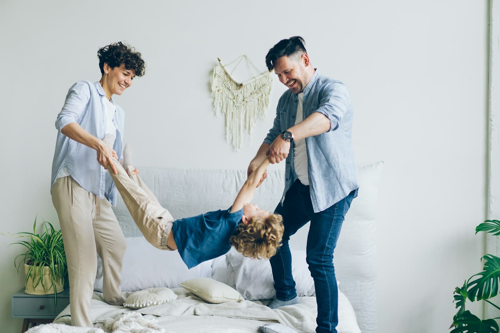 Two parents playfully swinging their young child between them in a bright room.